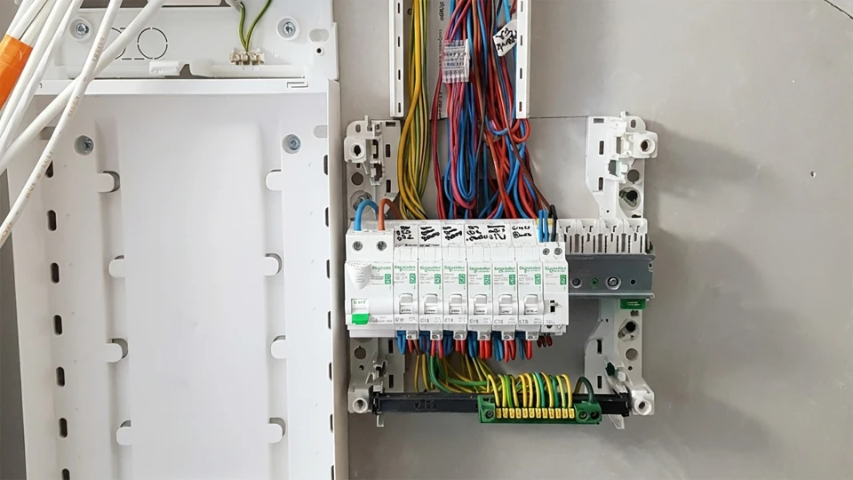 Électricien professionnel travaillant sur installation électrique murale intérieure, portant gants de sécurité orange et noir