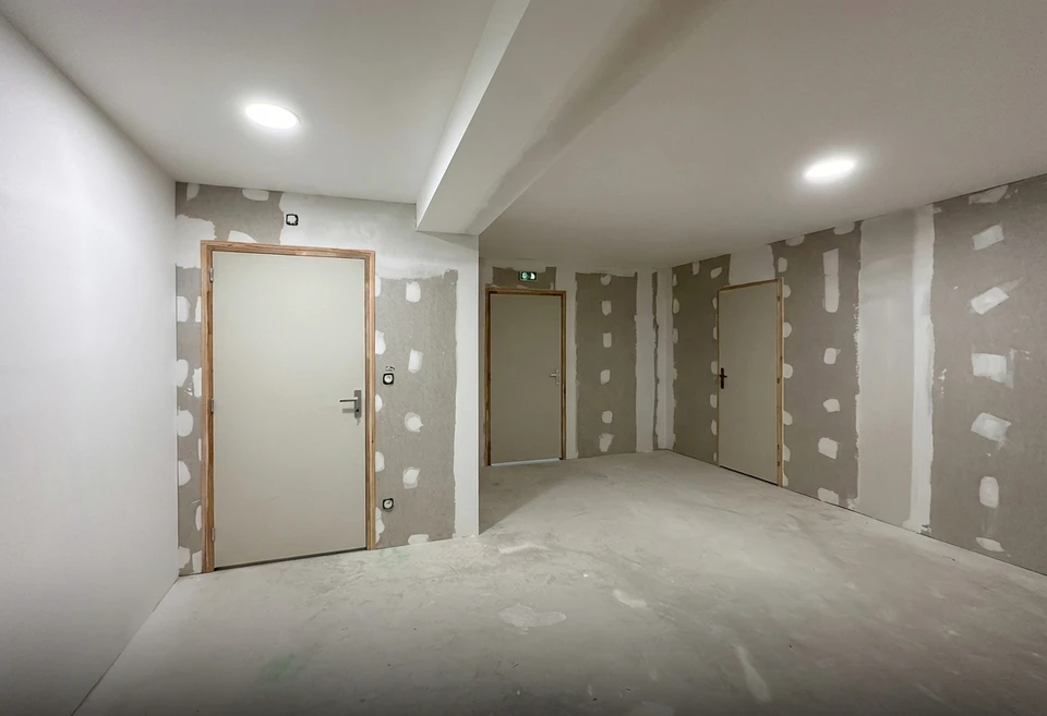 Deux ouvriers du bâtiment installent un faux plafond en plaques de plâtre dans un espace intérieur en construction