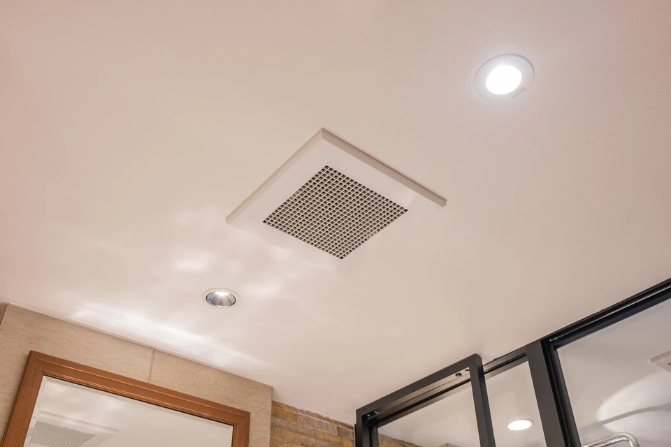 Ouvrier en combinaison à carreaux travaille dans les combles d'une habitation, installant ou réparant un système de ventilation