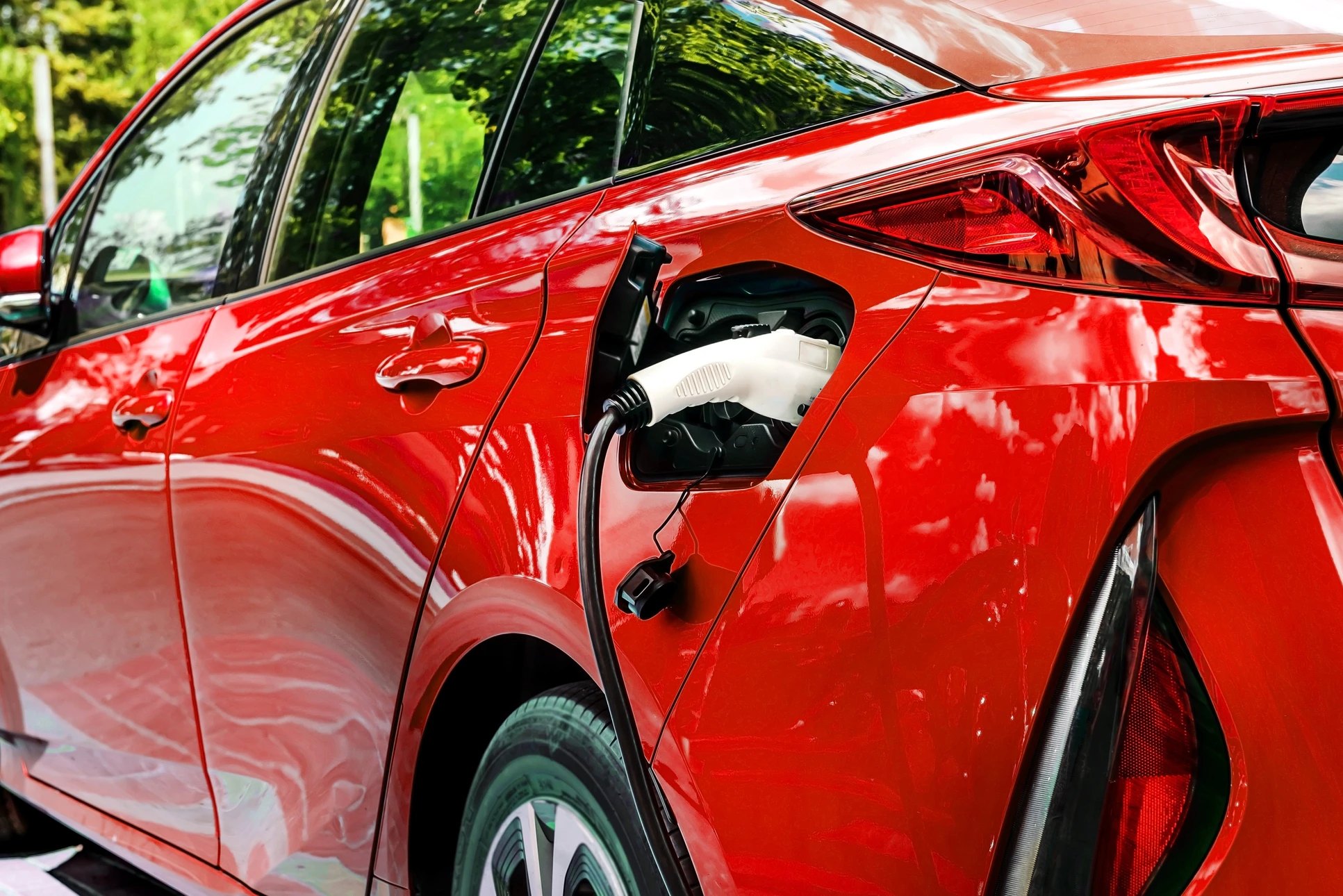 Scène extérieure avec véhicule électrique blanc en charge, câble d'alimentation jaune connecté au port de recharge latéral