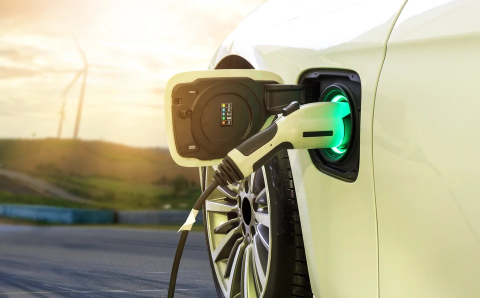 Scène extérieure montrant une voiture électrique blanche connectée à une borne de recharge sur route goudronnée